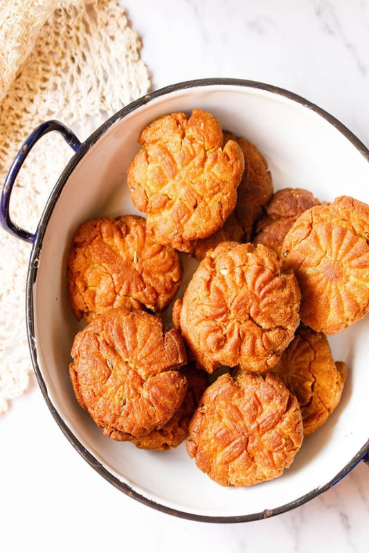 Round cookies with a textured surface in a white bowl with blue rim on a marble background